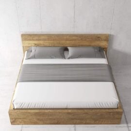 A neatly made Lugano Bed with a wooden frame, adorned with white bedding, gray pillows, and a matching gray blanket, set against a plain wall.