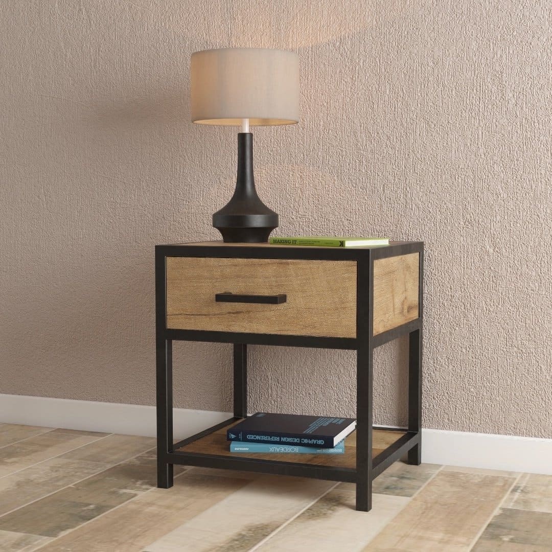 Urban Woodcraft Opus 24 Bed Side Table – MultiColoured Lifestyle An Opus Bedside End Table with a drawer and a shelf holding books, featuring a black base. A black lamp with a beige shade is placed on top of the table against a textured wall.