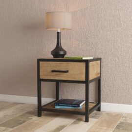 An Opus Bedside End Table with a drawer and a shelf holding books, featuring a black base. A black lamp with a beige shade is placed on top of the table against a textured wall.