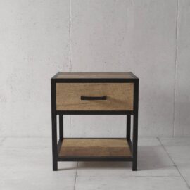 An *Opus Bedside End Table* with a black frame, a wooden top, one drawer with a handle, and an open lower shelf, set against a plain concrete wall.