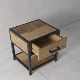 The Opus Bedside End Table is a wooden side table with a metal frame, featuring one open drawer and a lower shelf.