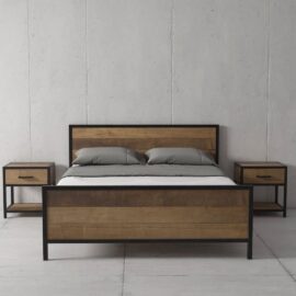 The Opus Bed, a modern wooden model featuring both a headboard and footboard, stands between two matching bedside tables. The bedding includes two gray pillows and a gray sheet, while the walls and floor are concrete.