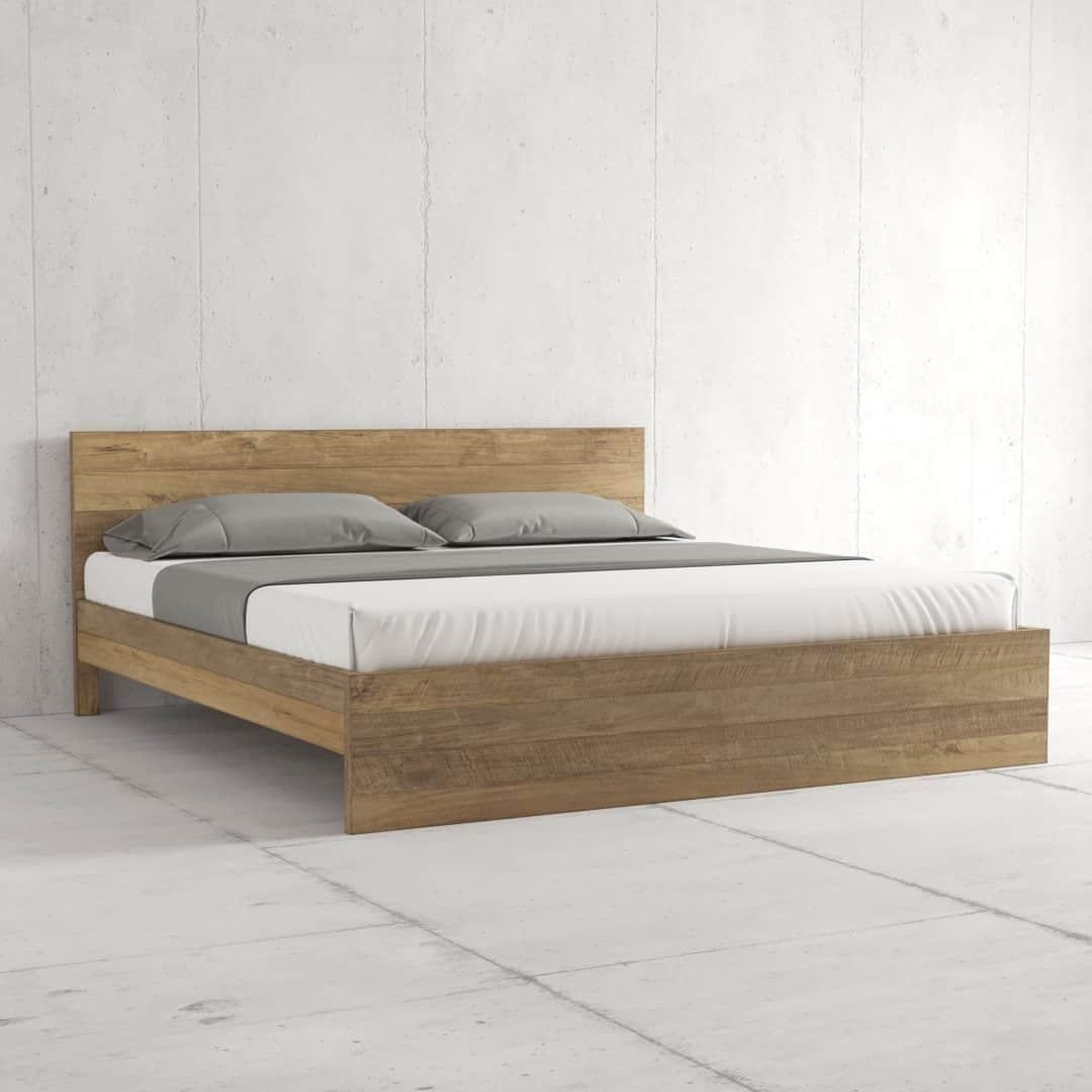 Urban Woodcraft Staillo Bed - Natural (4) The Satillo Bed, a minimalist wooden bed frame with a headboard, features two pillows on a neatly made bed adorned with white sheets and grey blankets, all set against a plain white wall.