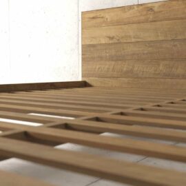 Satillo Bed, featuring a wooden frame with slats and a wooden headboard, set against a plain white wall.