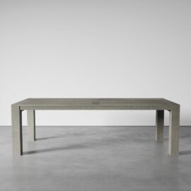 A Villa Dining Table - Natural stands on a smooth, gray concrete floor within a minimalist setting.