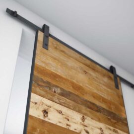 A close-up of the Maison 83" x 40" Barn Door on a metal sliding track system installed on a white wall.