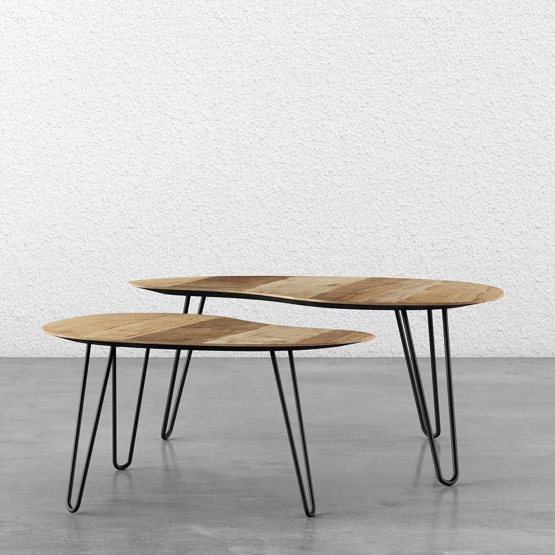 Two organic coffee tables crafted from multicolored teak, both featuring black metal hairpin legs. One is slightly larger than the other, positioned on a concrete floor against a white textured wall.
