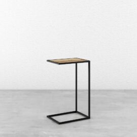A Side Table with a black metal frame and light wood top, positioned against a white textured wall on a smooth grey floor.