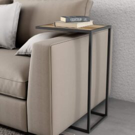 A Side Table featuring a black metal frame and a wooden top holds two books, positioned next to a beige sofa adorned with white and gray cushions.