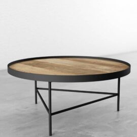 A Round Coffee Table featuring a wooden top and black metal frame, placed on a gray floor and positioned against a white wall.