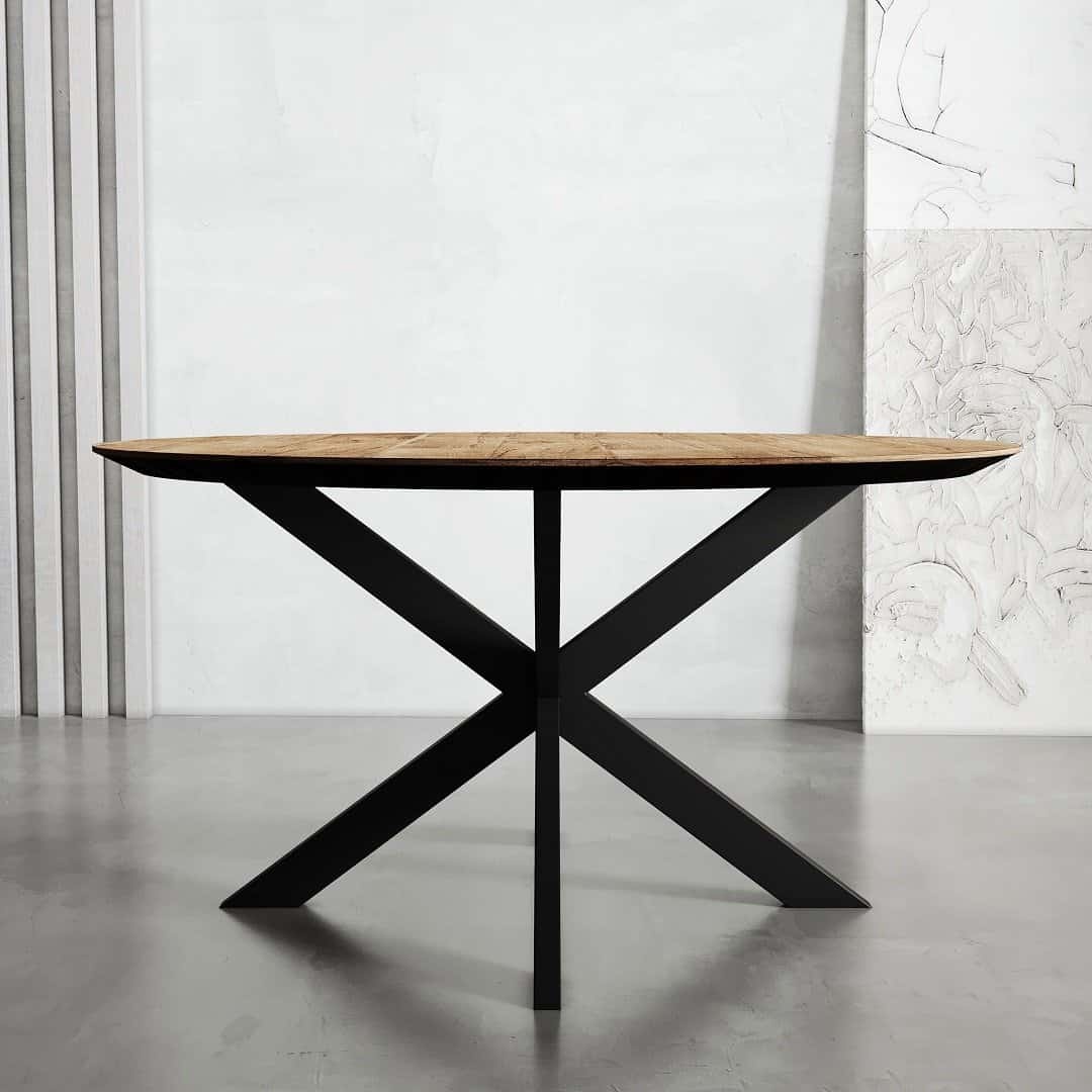 A wooden-topped round dining table with a black metal X-shaped base stands against a minimalist background with vertical lines and wall art, exuding the elegance of Kolt design.