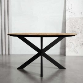 A wooden-topped round dining table with a black metal X-shaped base stands against a minimalist background with vertical lines and wall art, exuding the elegance of Kolt design.