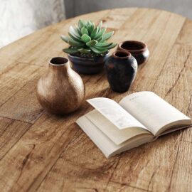 Open book on an Oval Kolt Dining Table with three small ceramic vases and a potted succulent plant.