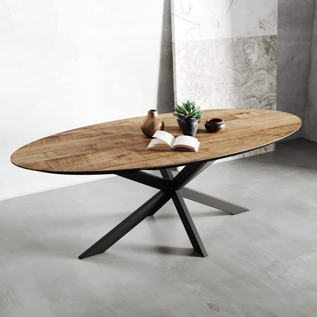 The Oval Kolt Dining Table, set on a gray floor and featuring a black metal base, showcases an open book, two vases, and a small potted plant.