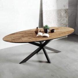 The Oval Kolt Dining Table, set on a gray floor and featuring a black metal base, showcases an open book, two vases, and a small potted plant.