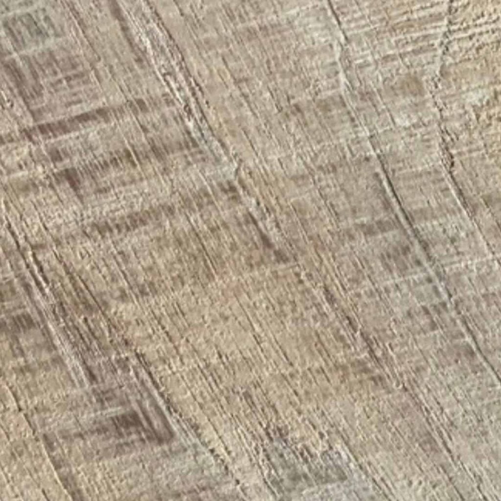 Close-up of a wooden surface showing light and dark grain patterns running diagonally with a slightly textured, worn appearance.