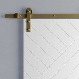 A white sliding barn door with the Meridian Hardware Kit, featuring brass accents and a diagonal panel design, is partially shown against a gray wall.