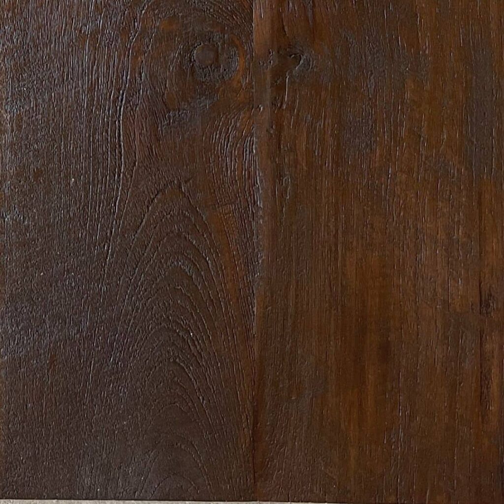 A close-up photograph of a dark brown wood texture with visible grain patterns and knots.