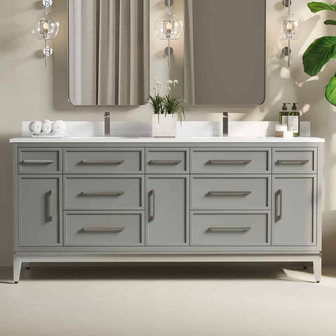 A modern Barrington bathroom vanity with a double sink, large mirrors, grey cabinets, and drawers. The setup includes soap dispensers, white rolled towels, and a potted plant.