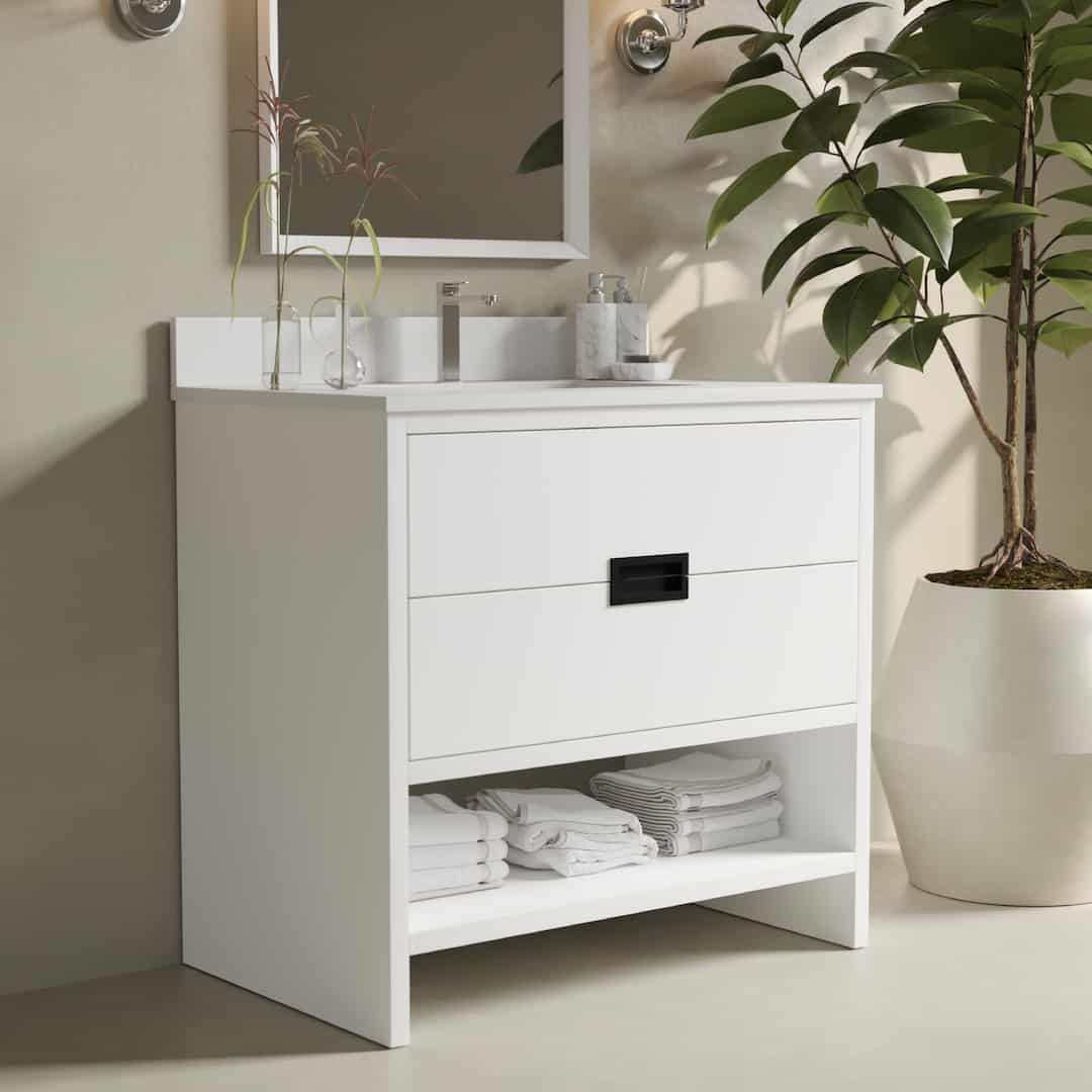 The Delamere 36" Single Sink Bathroom Vanity features a mirror above, an integrated sink, and a faucet. The drawer is accented with a black handle, while the open shelf below neatly stores folded towels. A potted plant is placed nearby for added décor.