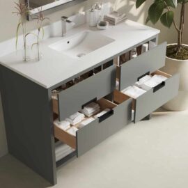The Delamere 48" Single Sink Bathroom Vanity features an integrated sink and three open drawers stocked with folded towels. A plant is placed beside the vanity, while toiletries are organized on the countertop.