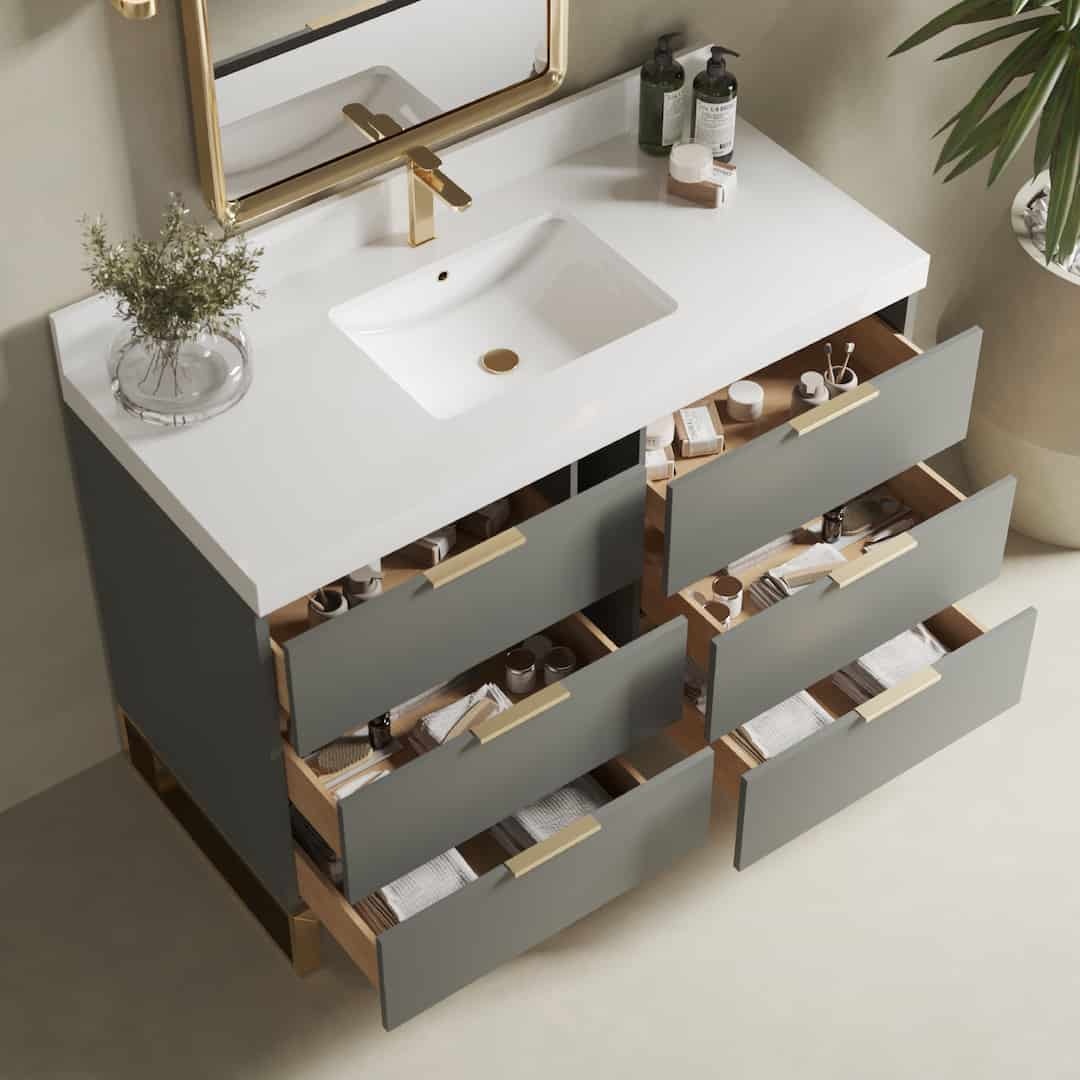 The Haldon 48" Single Sink Bathroom Vanity features a modern design with a white countertop, rectangular sink, brass faucet, gold-framed mirror, and six open drawers filled with toiletries. A green plant is placed on the right side for an added touch of freshness.