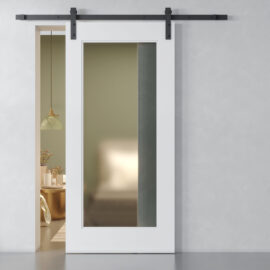 A Lucas 83" x 40" Reclaimed Wood Arrow Barn Door with a large glass panel is partially open, revealing a glimpse of a bedroom with green walls, a bed, and a side table holding a hanging lamp.