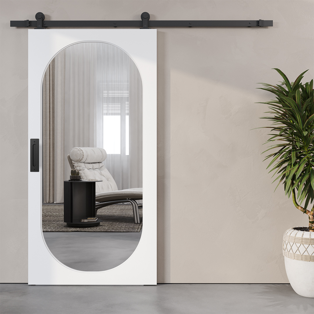The Celine 83" x 40" Oval Mirror Barn Door, in a sleek white finish, features an oval glass pane that reveals a modern interior with a stylish white lounge chair and a sunlit window. A potted plant is positioned next to the door on the right.