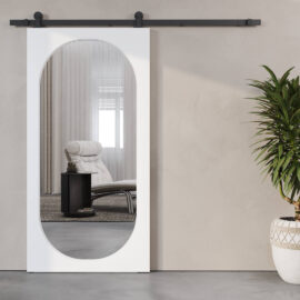 A modern Celine 83" x 40" Oval Mirror Barn Door reflects a minimalist room interior featuring a lounge chair and ottoman, next to a potted plant.