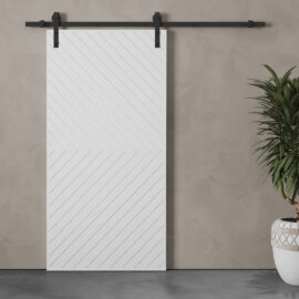 The Venice 83" x 40" Arrow Barn Door, featuring a white finish with diagonal striped patterns, is mounted on a sleek black track system against a beige wall. A green potted plant sits to the right of the door.
