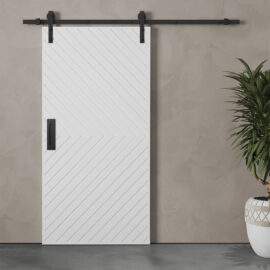 The Venice 83" x 40" Arrow Barn Door, featuring a chevron pattern, is mounted on a black track against a gray textured wall. A potted plant is placed on the right side.