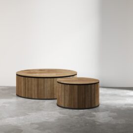 Two Bolivar Coffee Tables with slatted sides and round, wooden tops stand on a concrete floor against a plain, light wall. The tables are of different heights.