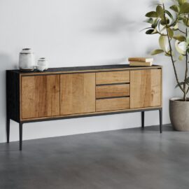 The Kolt 3 Door Dining Buffet, a modern wooden sideboard with a black top and base, featuring two cabinets and three drawers, stands on a grey floor next to a potted plant and two ceramic vases.