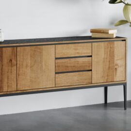 The Kolt 3 Door Dining Buffet, with a black top and legs, featuring two cabinets and two drawers, is set against a white wall with a few books and a green plant on top.