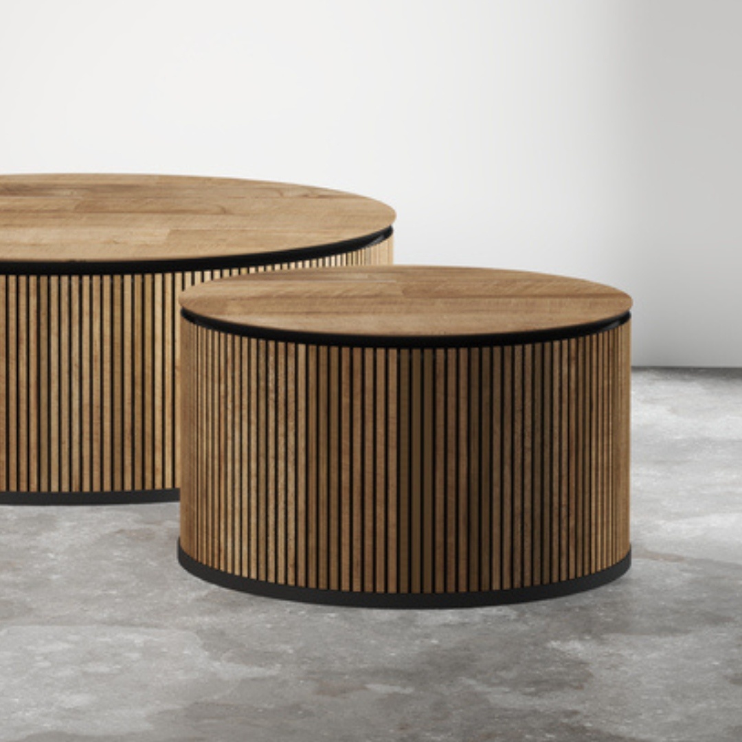 Two Bolivar Coffee Tables with round wooden surfaces and vertical slat detailing, placed on a concrete floor in front of a plain wall.