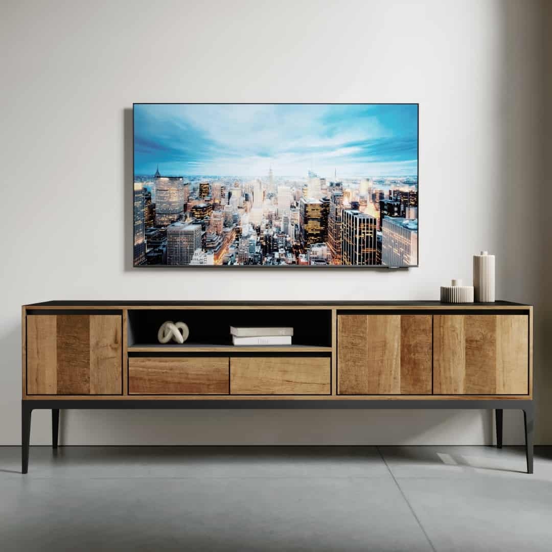 68 KOLT WIDE TV STAND – 3 The Kolt 60" Wide TV Stand, featuring a modern wooden design with black legs, is placed against a white wall, adorned with decor items. Above it, a large flat-screen TV showcases a cityscape.