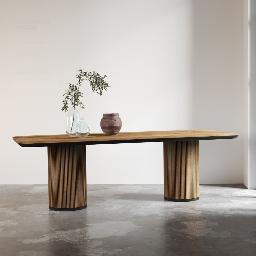 88 Bolivar DT (2) A Bolivar Rectangle Dining Table with cylindrical legs holds a glass vase with green branches and a pinkish-brown ceramic pot in a minimalist room with concrete flooring.