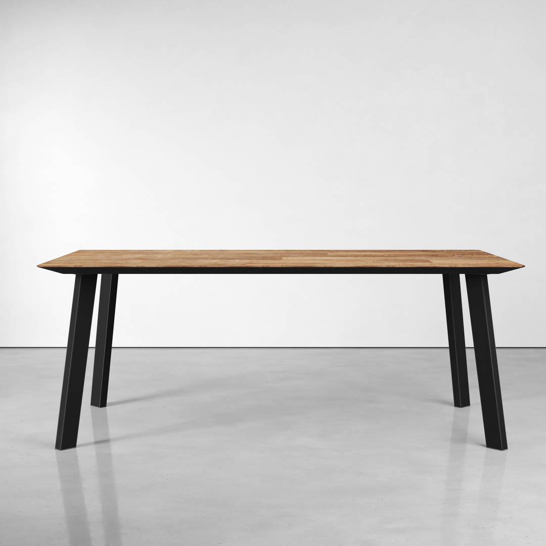 The Rectangle Kolt Dining Table, featuring a simple rectangular wooden top and four black metal legs, is placed on a gray floor against a plain white wall.