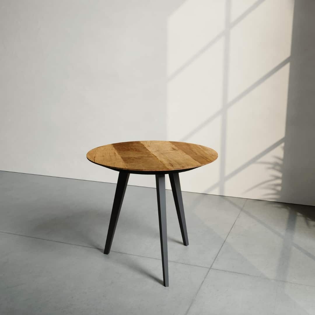 The Round Kolt Coffee Table, featuring a wooden surface and three black legs, stands on a gray floor near a wall with a window that casts shadows.