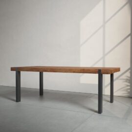 A Beam Dining Table with metal legs stands in a sunlit, minimalist room with smooth, light-colored walls and a large window casting shadows on the floor.