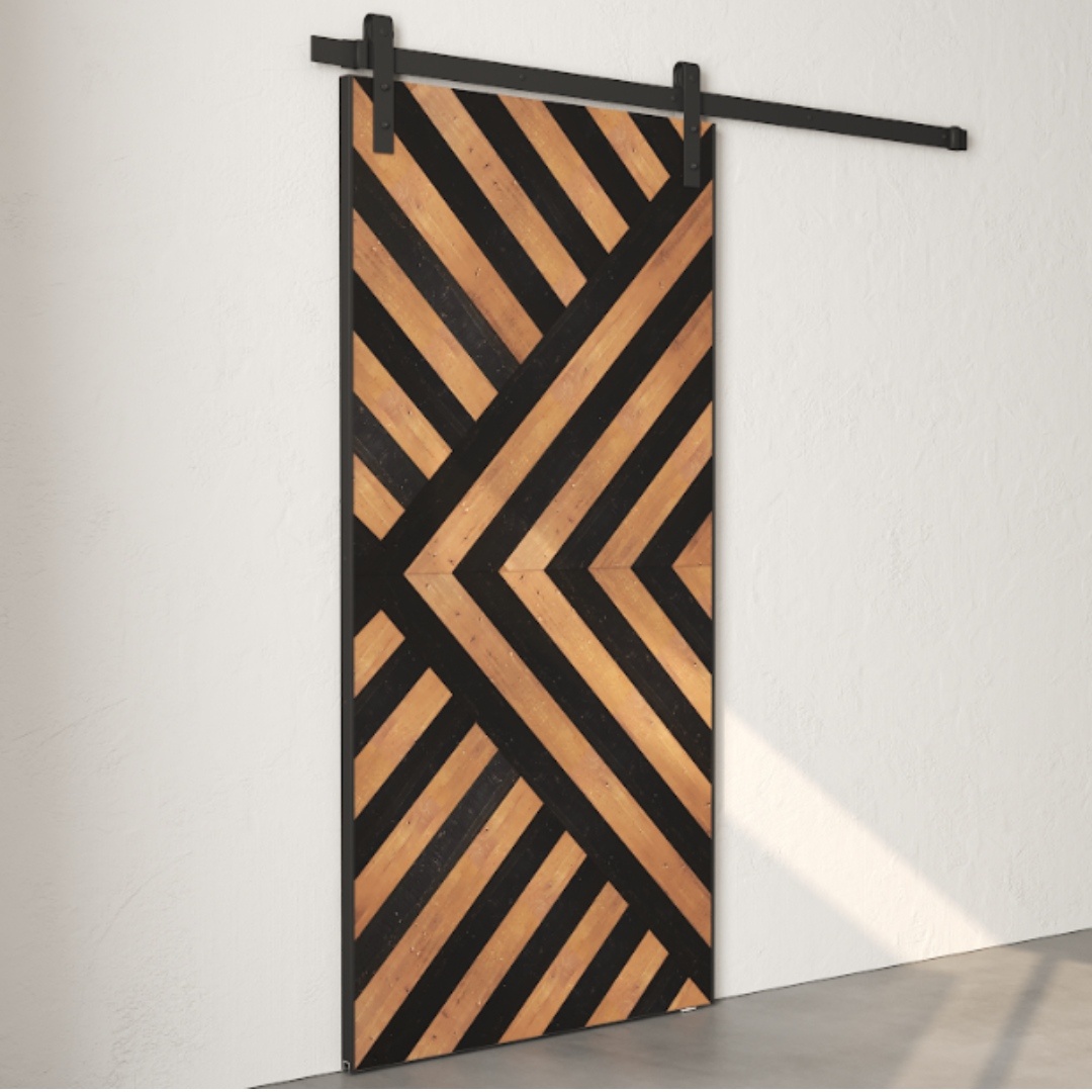 The Enigma Reclaimed Wood Barn Door Espresso, featuring a geometric pattern of diagonal black and wood stripes, is mounted on a white wall.