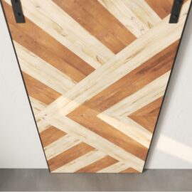 The Lumina Reclaimed Wood Barn Door White, featuring a chevron pattern crafted from alternating light and dark wood panels, is mounted on a wall.