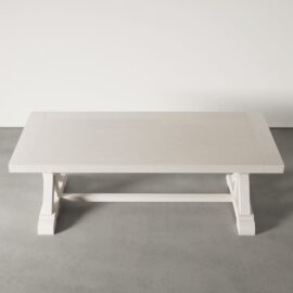 A Pure White Madera Dining Table with crossbar support, placed on a gray concrete floor against a white wall.
