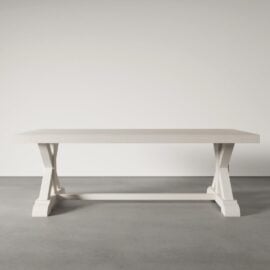 The Madera Dining Table - Pure White, featuring a rectangular design and an X-shaped base, stands on a gray concrete floor against a plain light-colored wall.