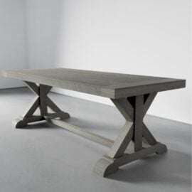 A sturdy, rectangular Madera Dining Table - Rustic Grey with an X-trestle base, placed in an empty room with light grey walls and a smooth floor.