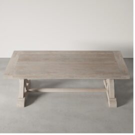 The Madera Dining Table - White Wash, a rectangular wooden dining table with a natural light finish, featuring a rustic design and sturdy base, is placed on a grey concrete floor against a plain white background.
