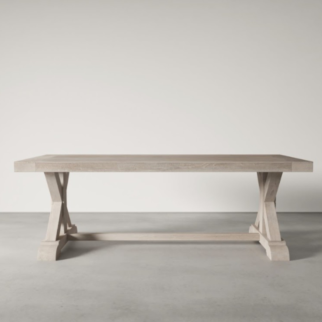 The Madera Dining Table - White Wash, featuring a trestle base and a rectangular top, sits elegantly on a light gray concrete floor.