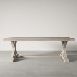 The Madera Dining Table - White Wash, featuring a trestle base and a rectangular top, sits elegantly on a light gray concrete floor.