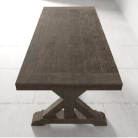 The Madera Dining Table - Café Noire, featuring a large, dark wooden surface and an X-shaped support base, stands on a white tiled floor in a bright room.