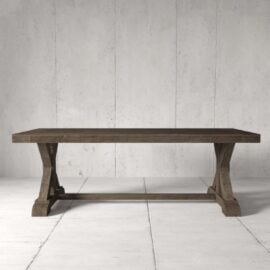 The Madera Dining Table - Café Noire, featuring sturdy, carved wooden legs, stands on a light, tiled floor against a concrete wall.